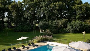 A swimming pool with lounge chairs and umbrellas, surrounded by a well-maintained lawn and trees.