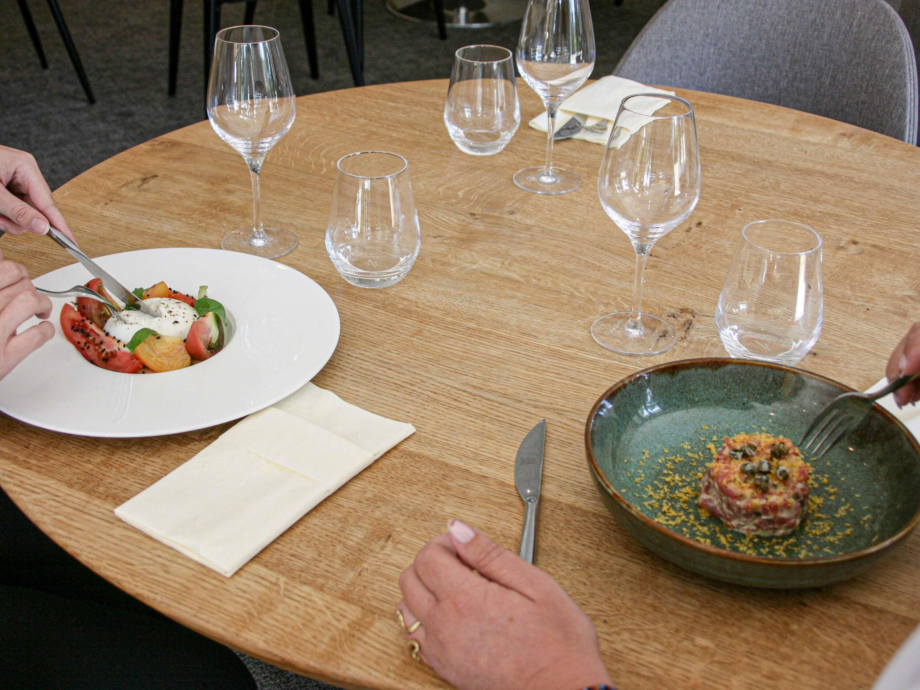 A round wooden table with a white plate of food, a green bowl with a sauce, and empty wine glasses.