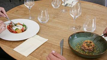 A round wooden table with a white plate of food, a green bowl with a sauce, and empty wine glasses.