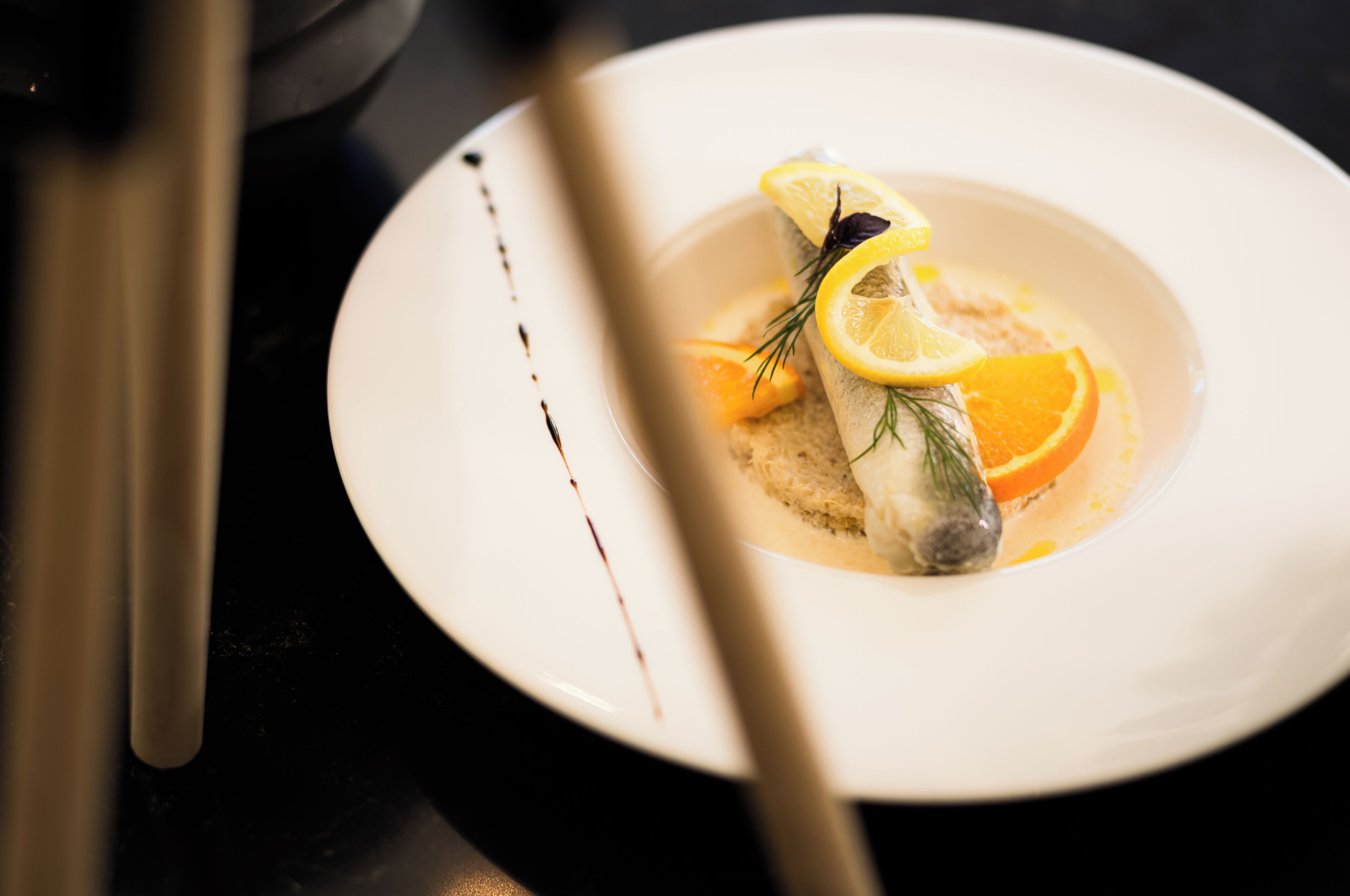 Un plato blanco con un guiso de pescado adornado con rodajas de limón y hierbas, acompañado de una cuchara.