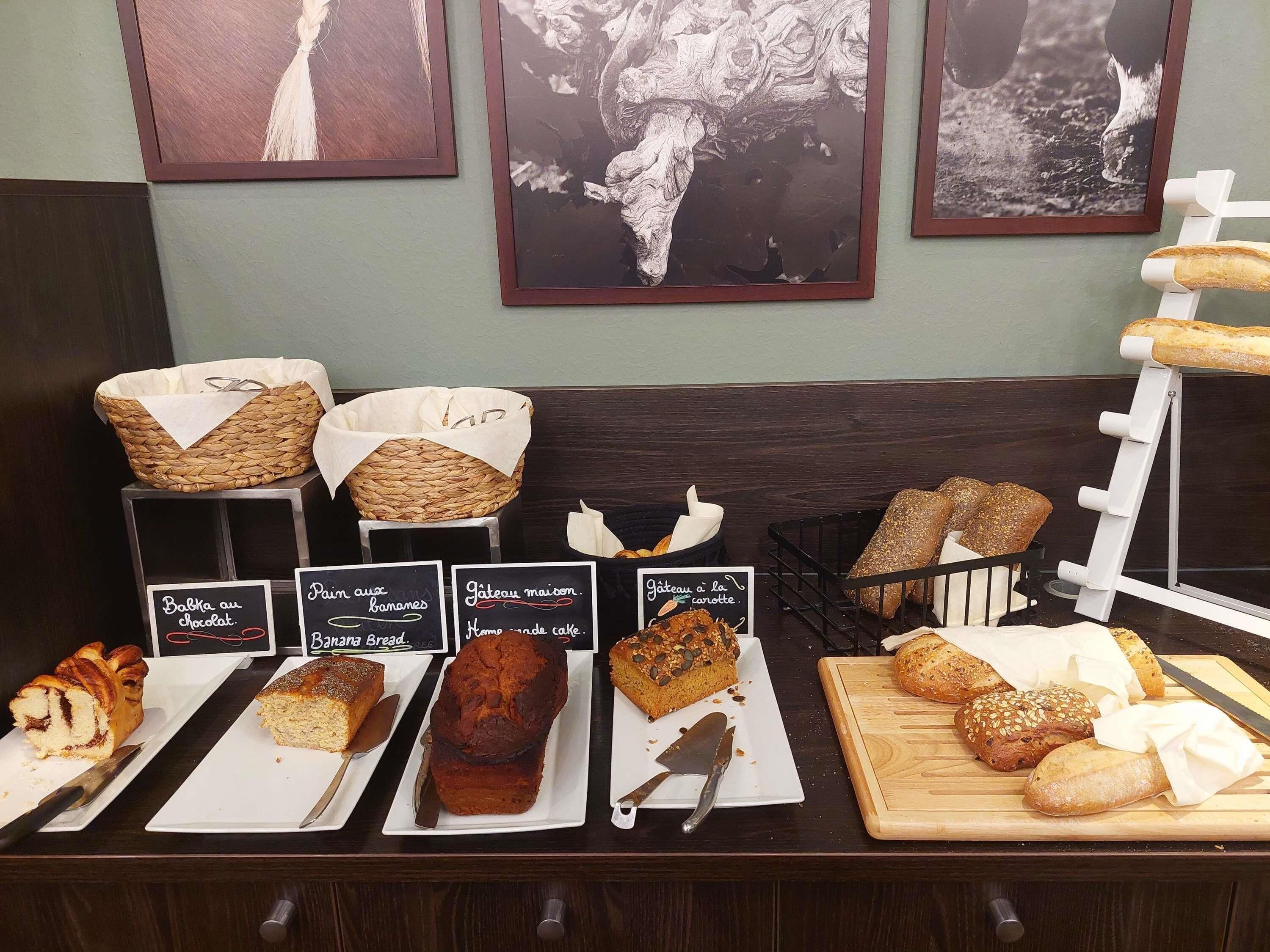 Une vitrine de boulangerie présentant diverses sortes de pains et de gâteaux, notamment du pain aux bananes et un gâteau décoré en forme de maison.