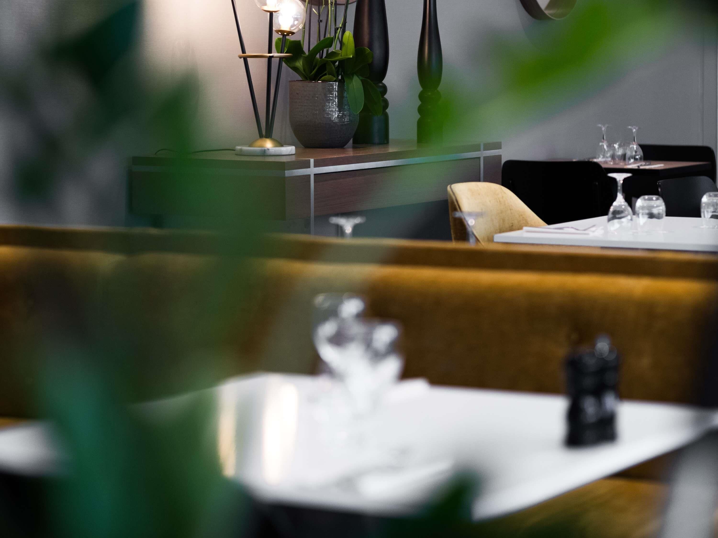 A restaurant interior with a dining table set for two, a vase with flowers, and a plant on the table.