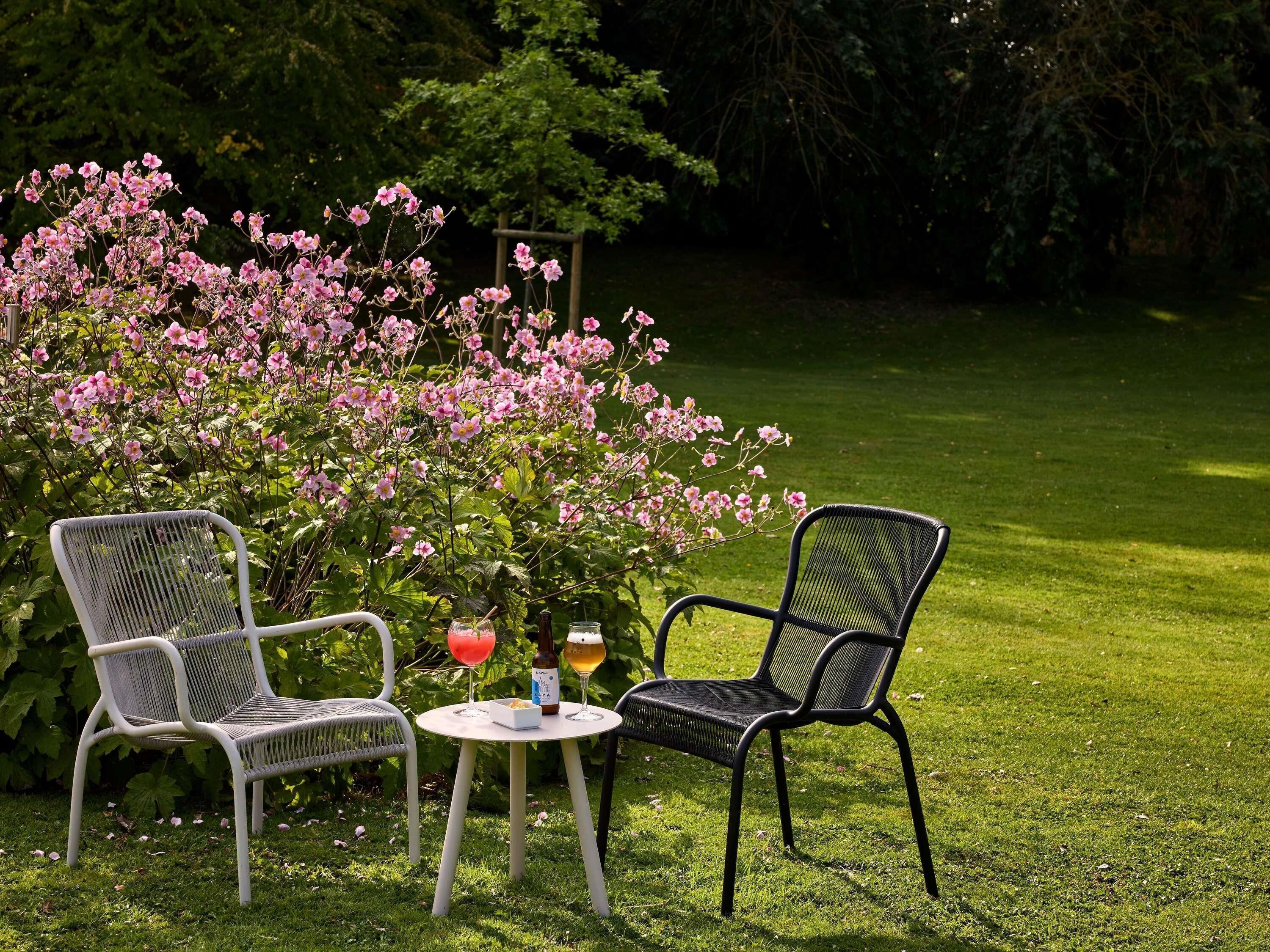 Dos sillas y una mesita con bebidas y una botella en un jardín.
