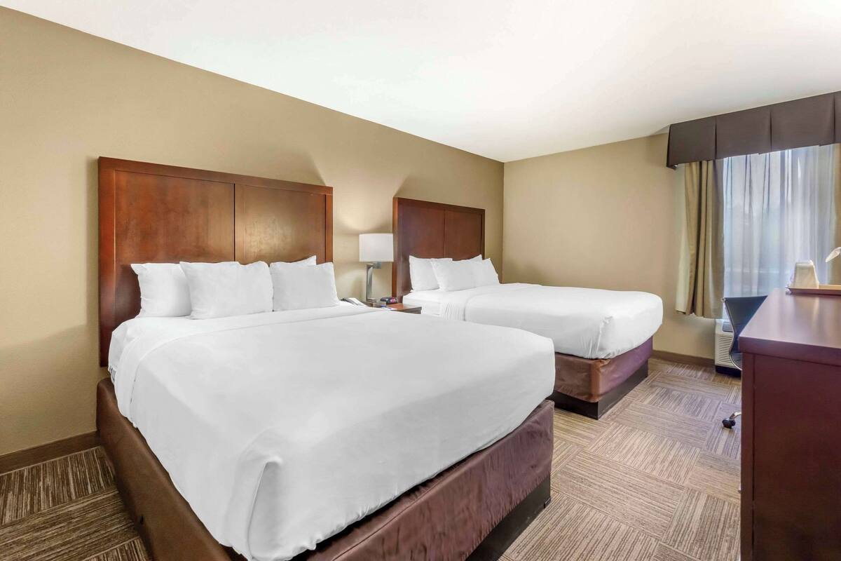 A hotel room with two beds, a desk, a lamp, and a window with curtains.