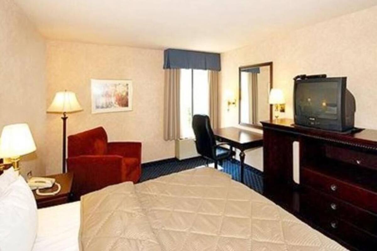 A hotel room with a bed, a desk, a chair, a television, and a lamp.