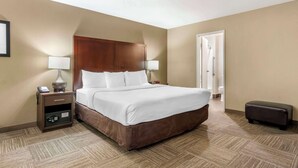 A hotel room with a large bed, bedside lamps, a nightstand with a phone and a safe, a small ottoman, and a door leading to a bathroom. - Comfort Inn & Suites Sea-Tac Airport (SeaTac)