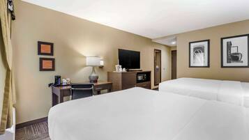 A hotel room with two beds, a desk with a lamp, a television, a microwave, and framed pictures on the wall.