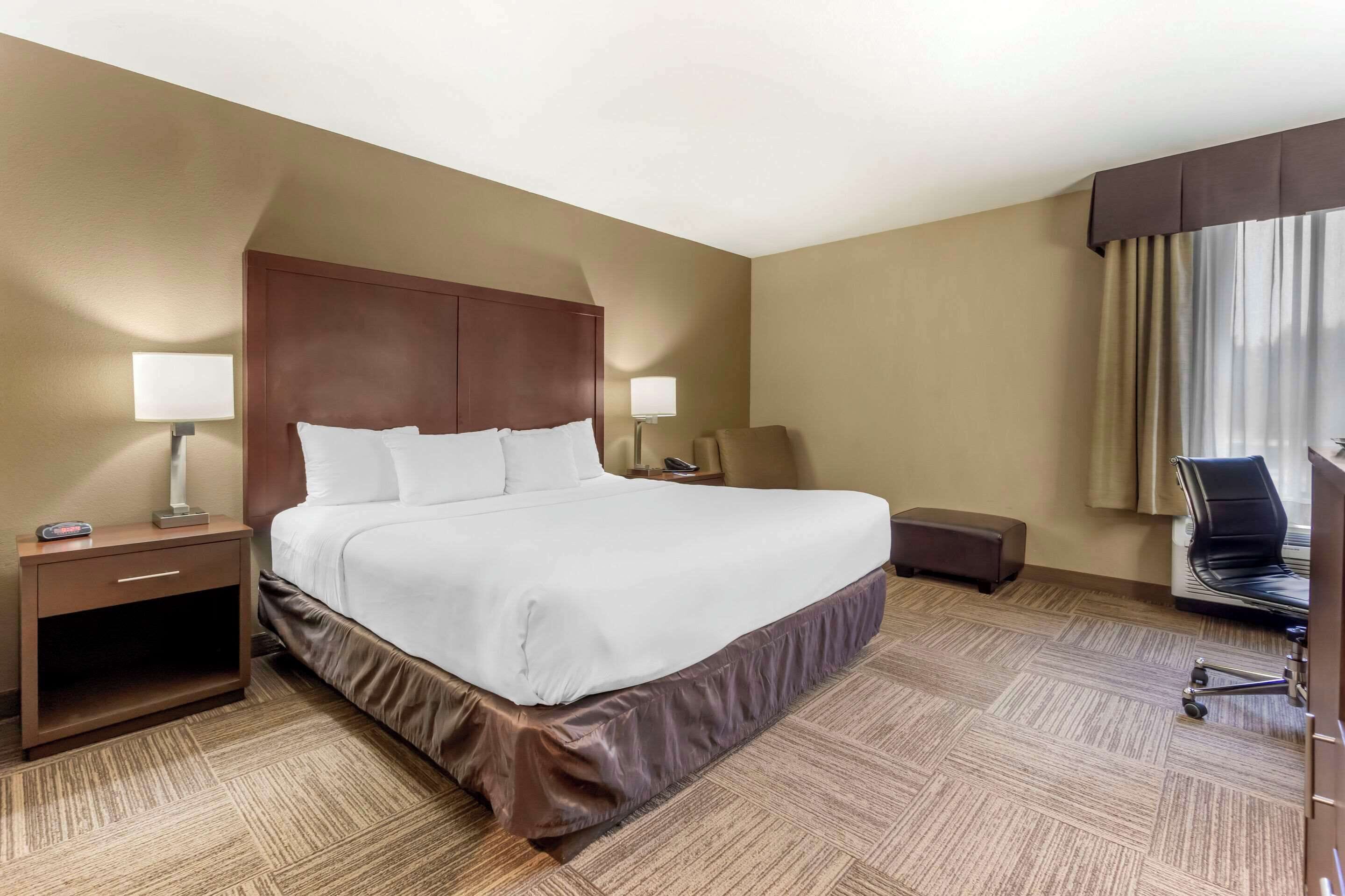A hotel room with a large bed, bedside tables, a desk, a chair, and a window with curtains.