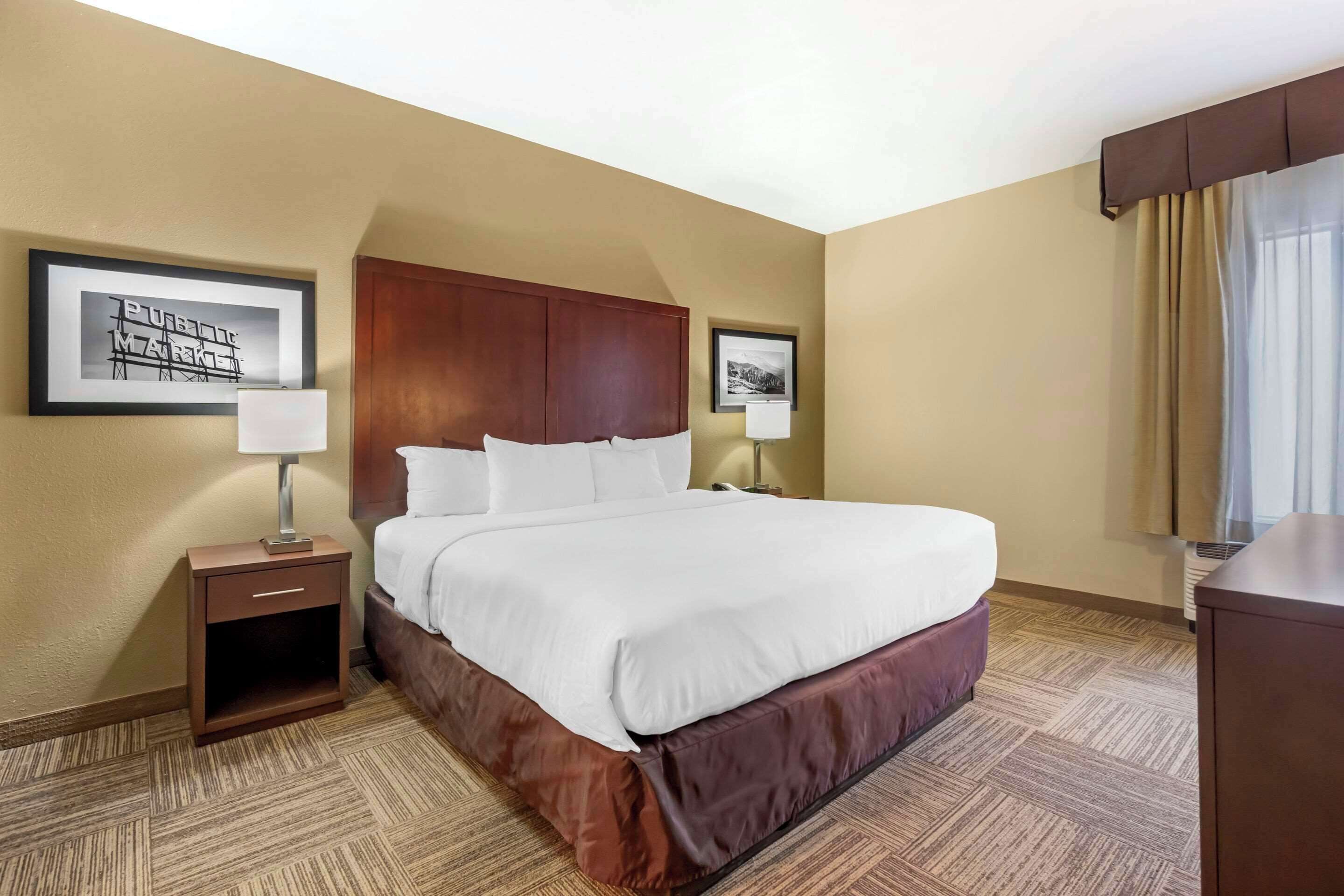 Habitación de hotel con una cama grande, una mesita de noche con lámpara y dos cuadros en las paredes.