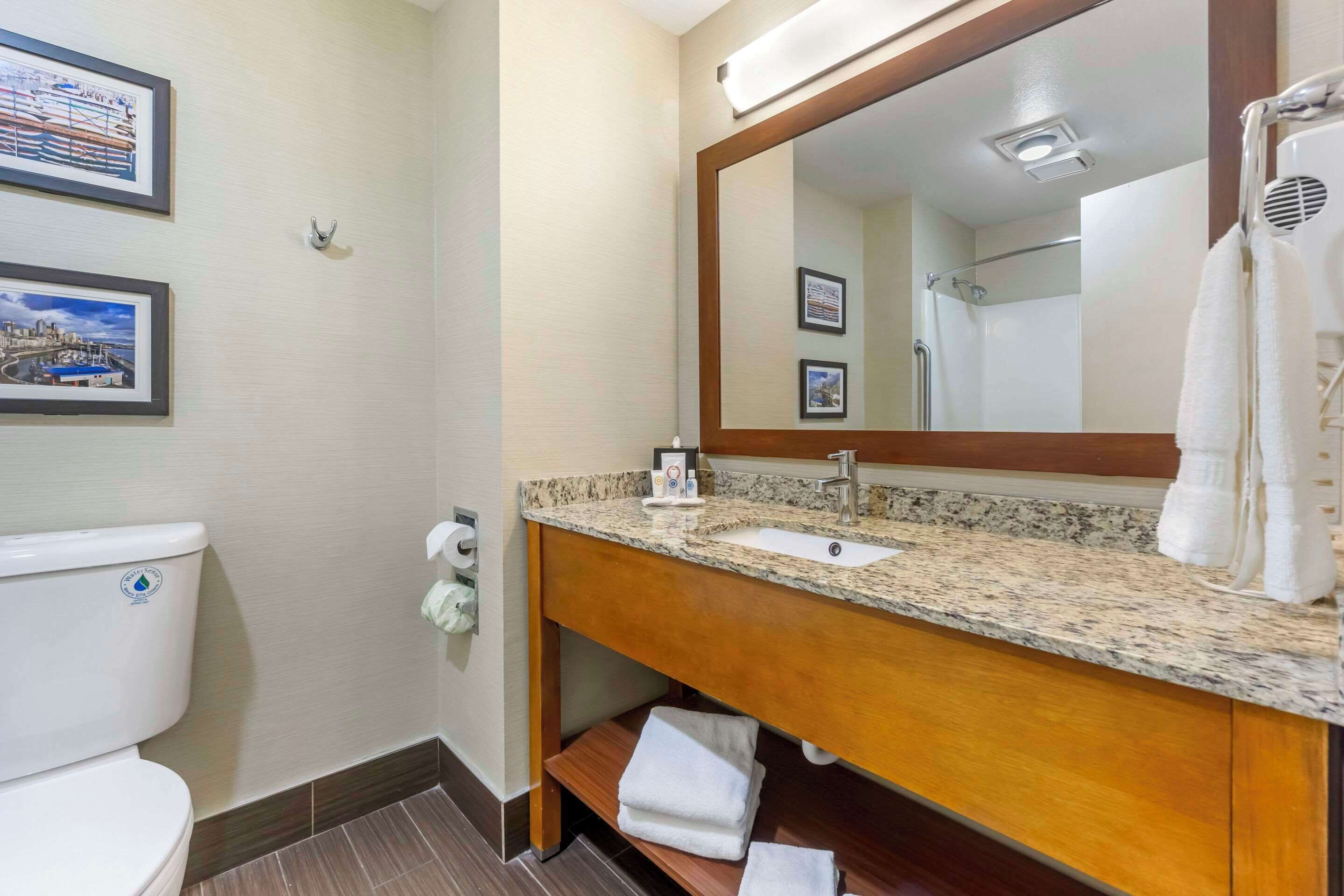 A bathroom with a toilet, sink, mirror, and framed pictures on the wall.