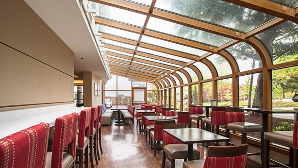 A restaurant with a glass roof, wooden tables, and red upholstered chairs. - Comfort Inn & Suites Sea-Tac Airport (SeaTac)
