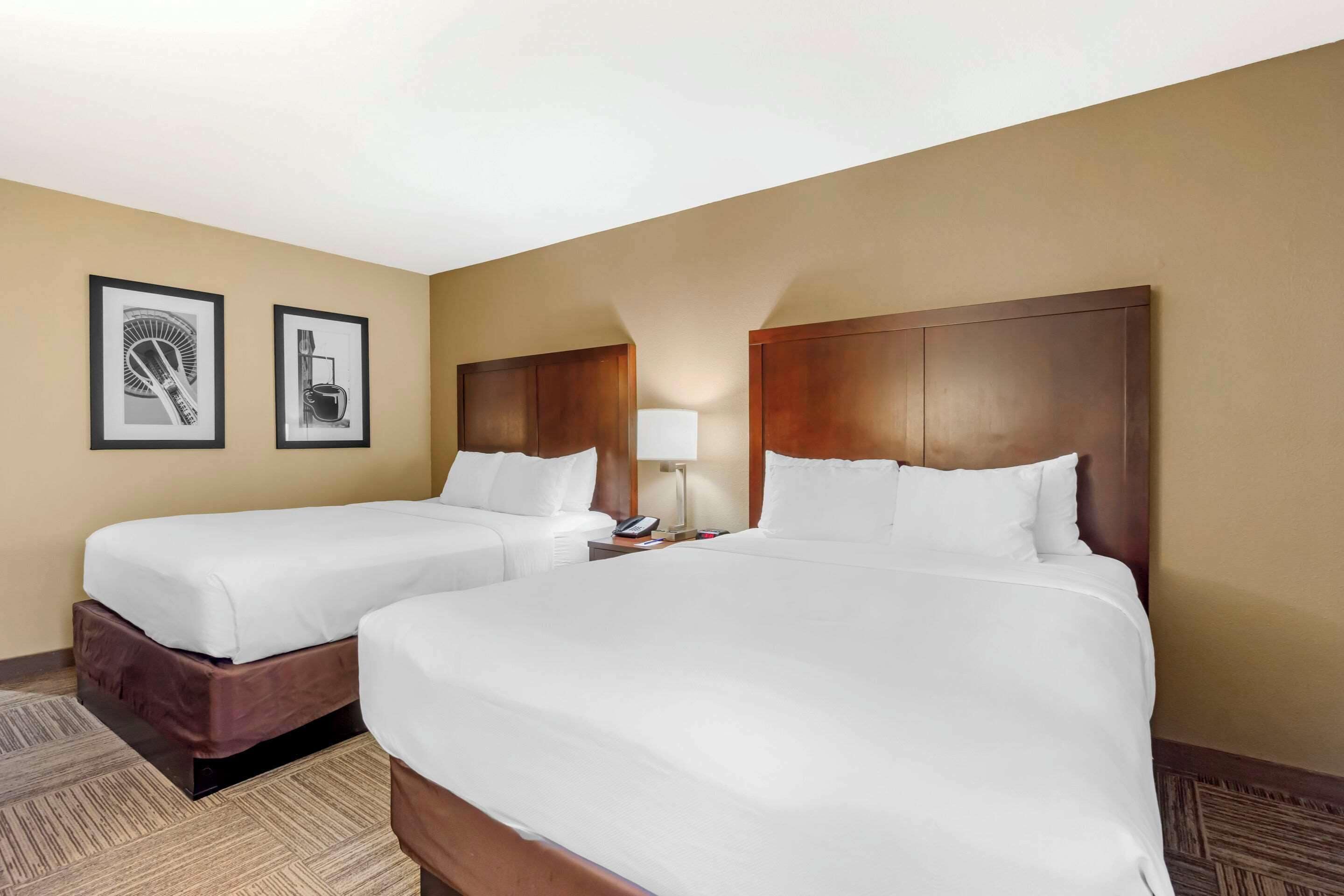 A hotel room with two single beds, a nightstand with a lamp, and two framed pictures on the wall.