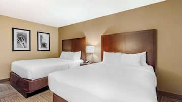 A hotel room with two single beds, a nightstand with a lamp, and two framed pictures on the wall.