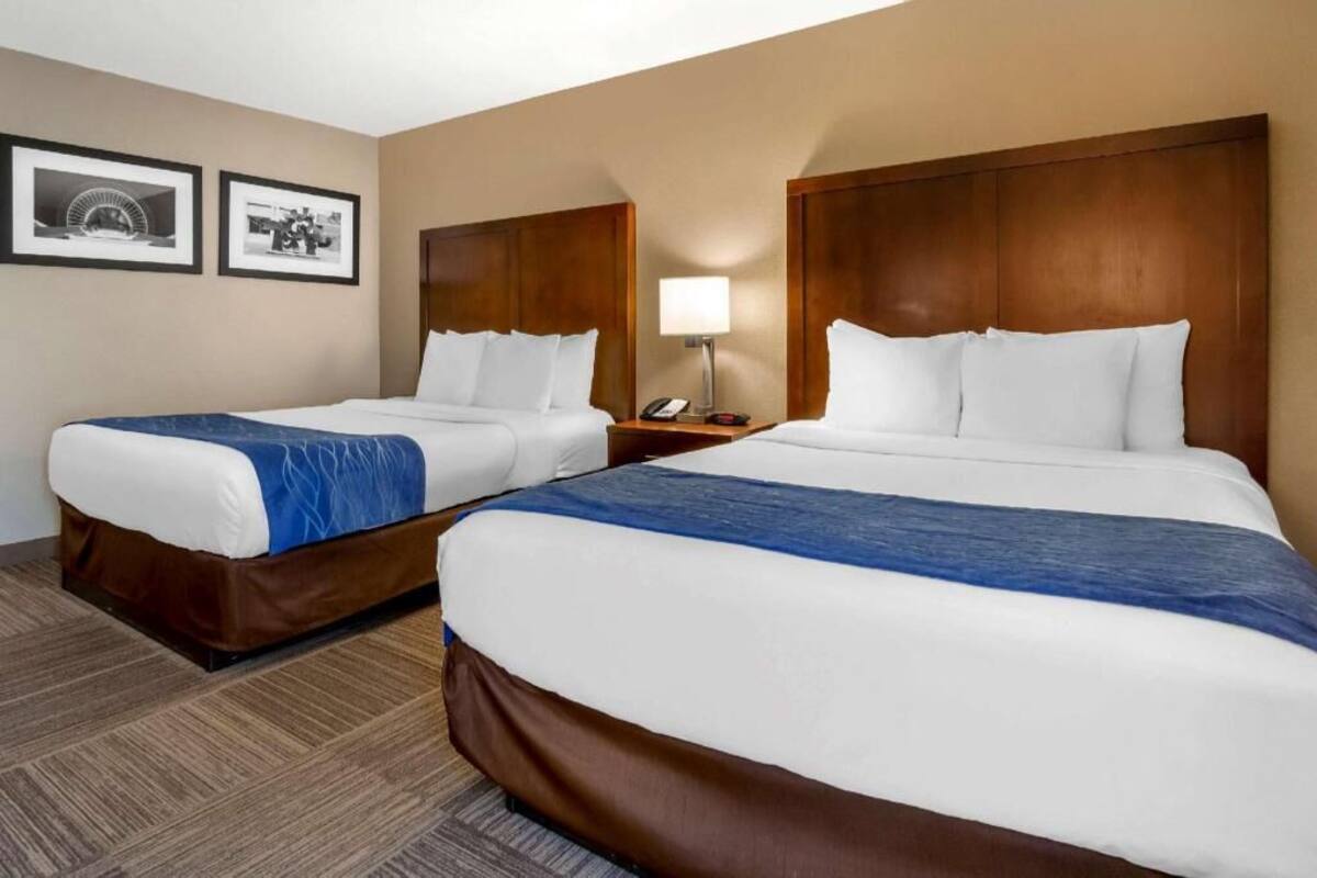 A hotel room with two beds, a nightstand with a lamp, and two framed pictures on the wall.