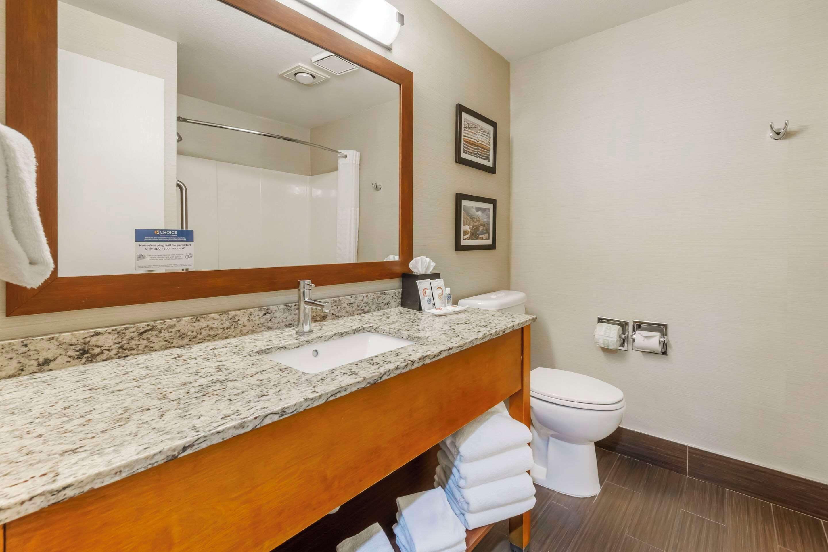 A bathroom with a granite countertop sink, a white toilet, and a large mirror.
