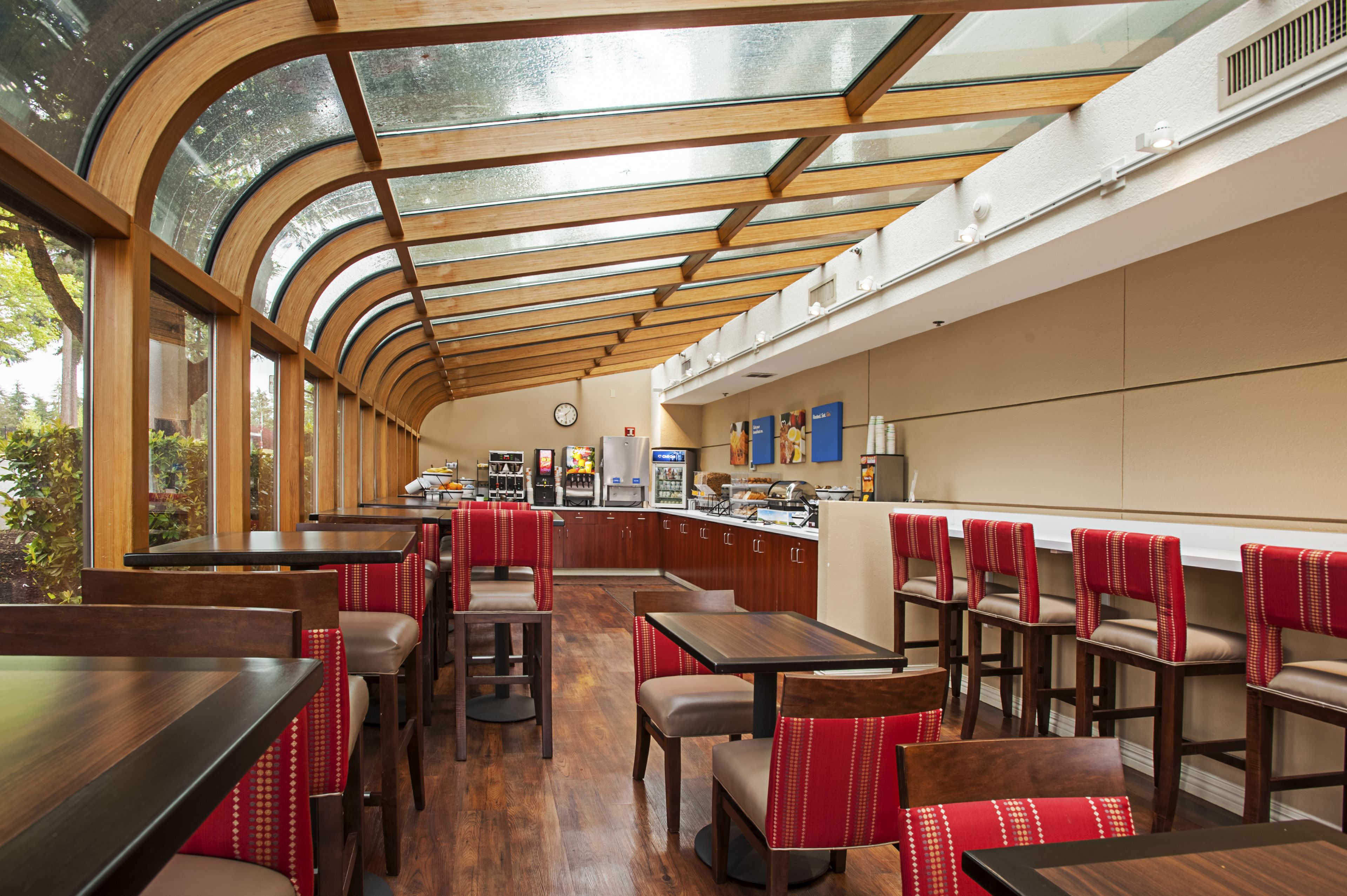 Un restaurant doté d’un plafond incurvé, de tables et de chaises en bois, et offrant une vue sur la verdure environnante.