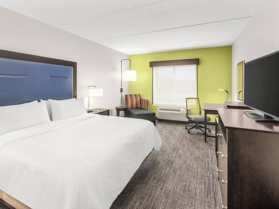 A hotel room with a large bed, a desk with a flat-screen TV, a chair, a lamp, and a window with a view.