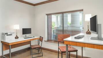 Habitación de hotel con escritorio, dos sillas, computadora, impresora y ventana con persianas.