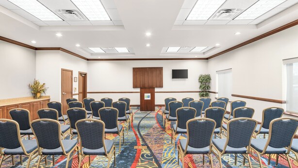 A conference room with rows of chairs, a podium, a flat-screen TV, and a large window. - Holiday Inn Express & Suites Wilmington-Newark by IHG  (Newark)