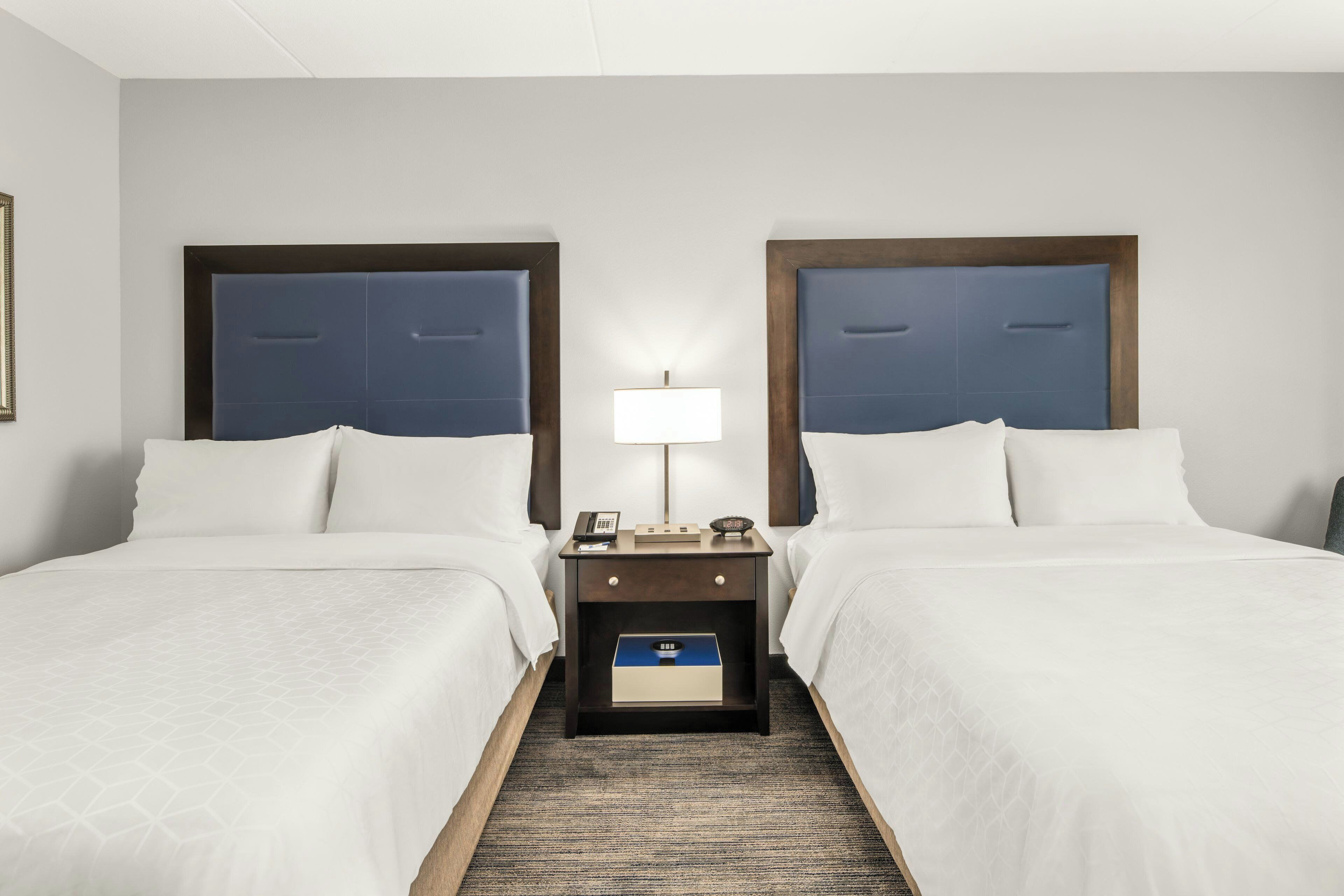 A hotel room with two beds, a nightstand with a lamp, and a small drawer unit.