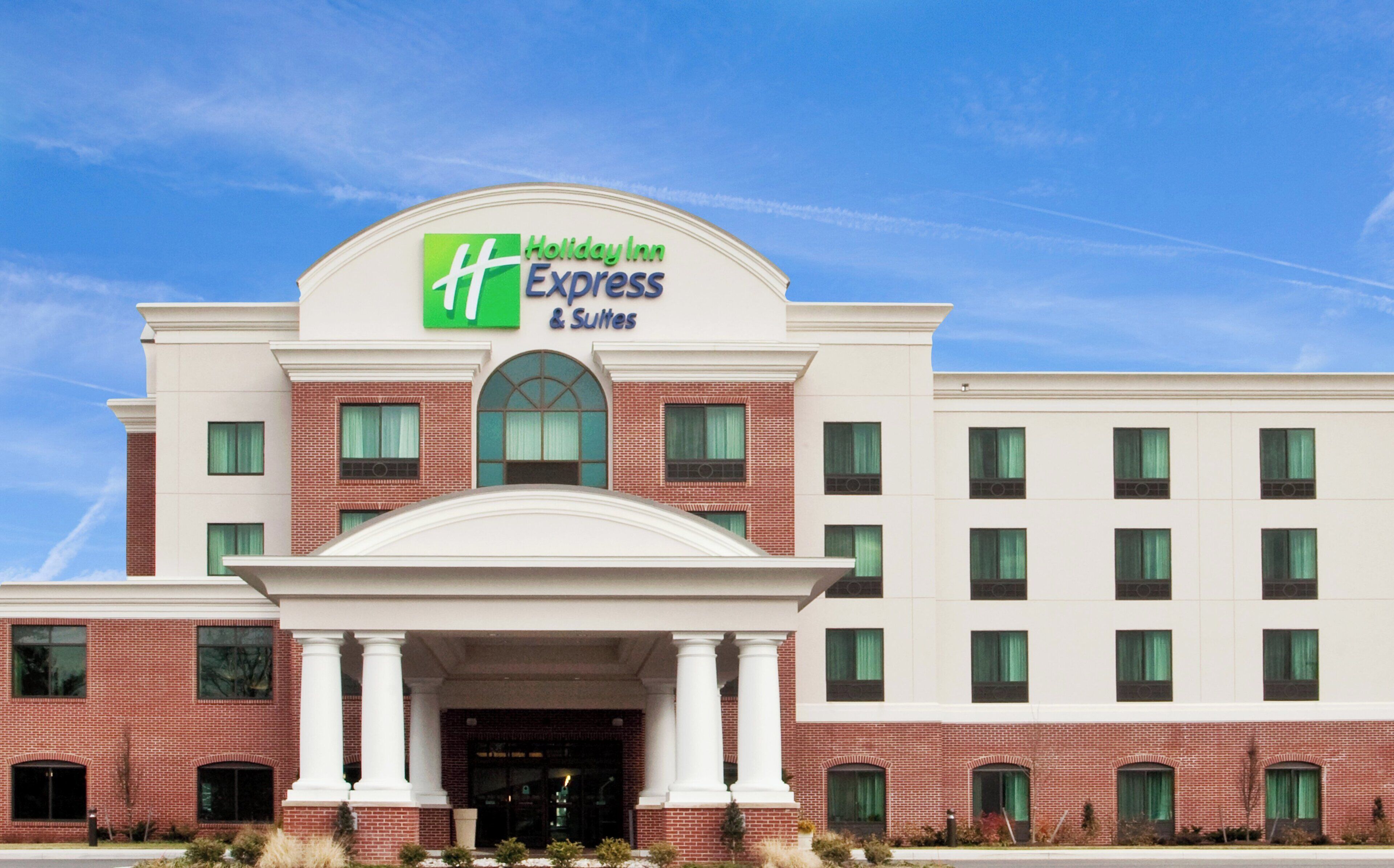 A Holiday Inn Express & Suites hotel with a symmetrical facade, large windows, and a central entrance with columns.