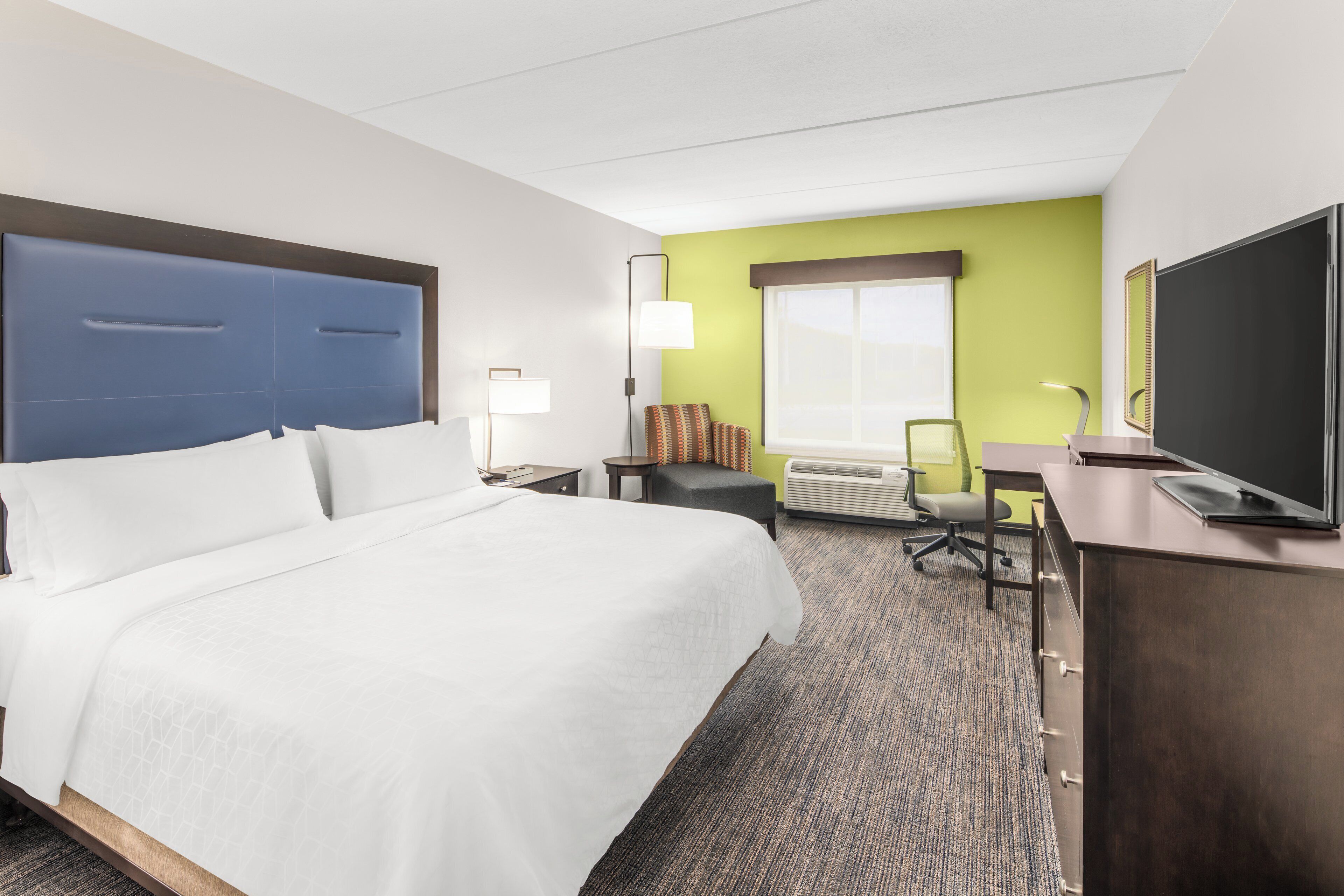 A hotel room with a large bed, a desk, a chair, a television, and a window with a view.