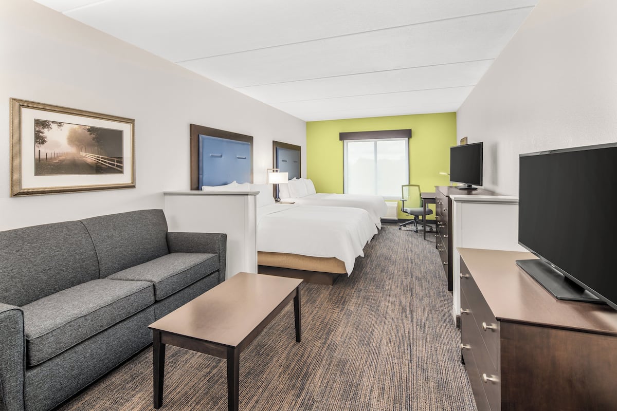 A hotel room with a sofa, a bed, a desk, a TV, and a framed picture on the wall.