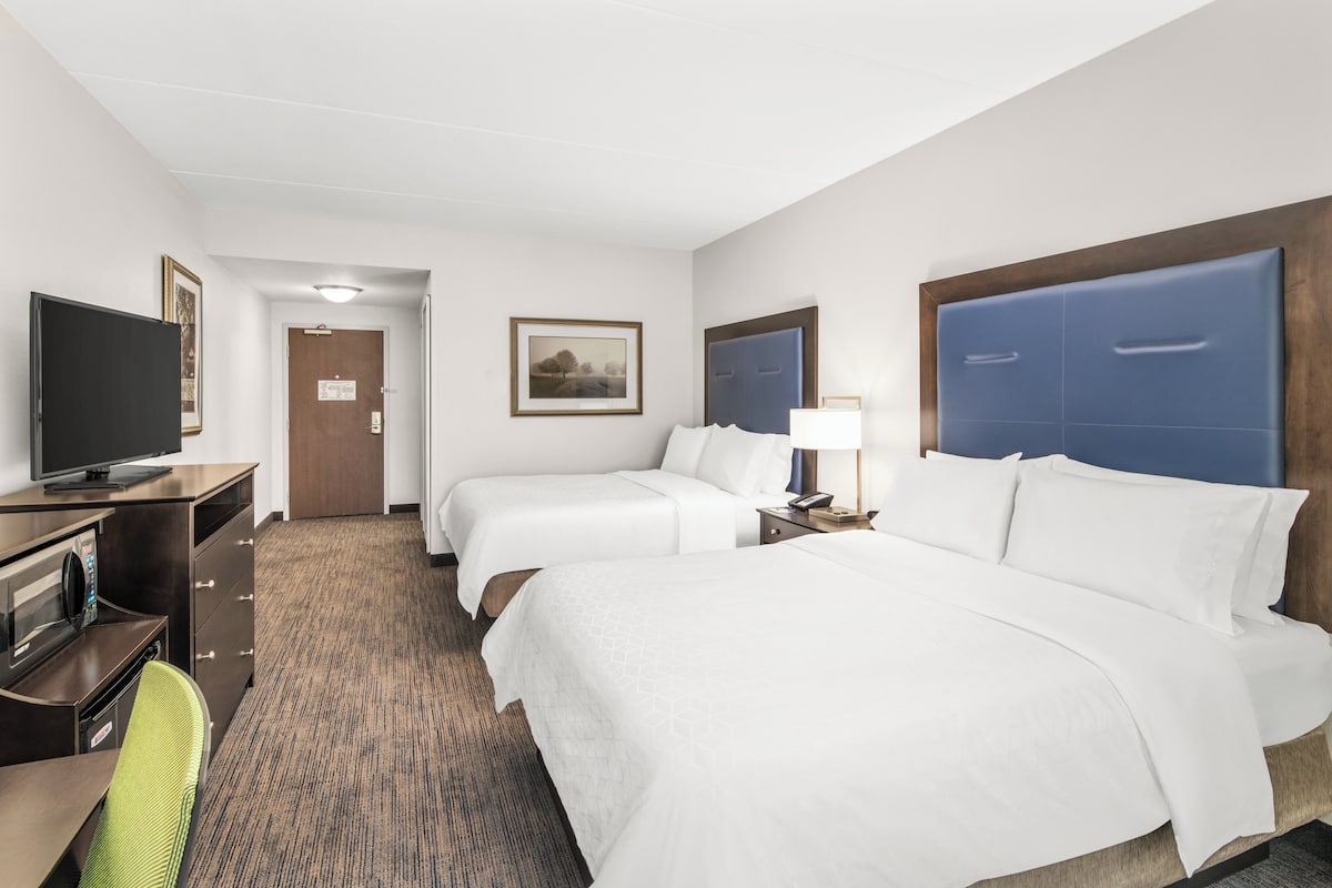 A hotel room with two beds, a desk with a television, a chair, and a carpeted floor.