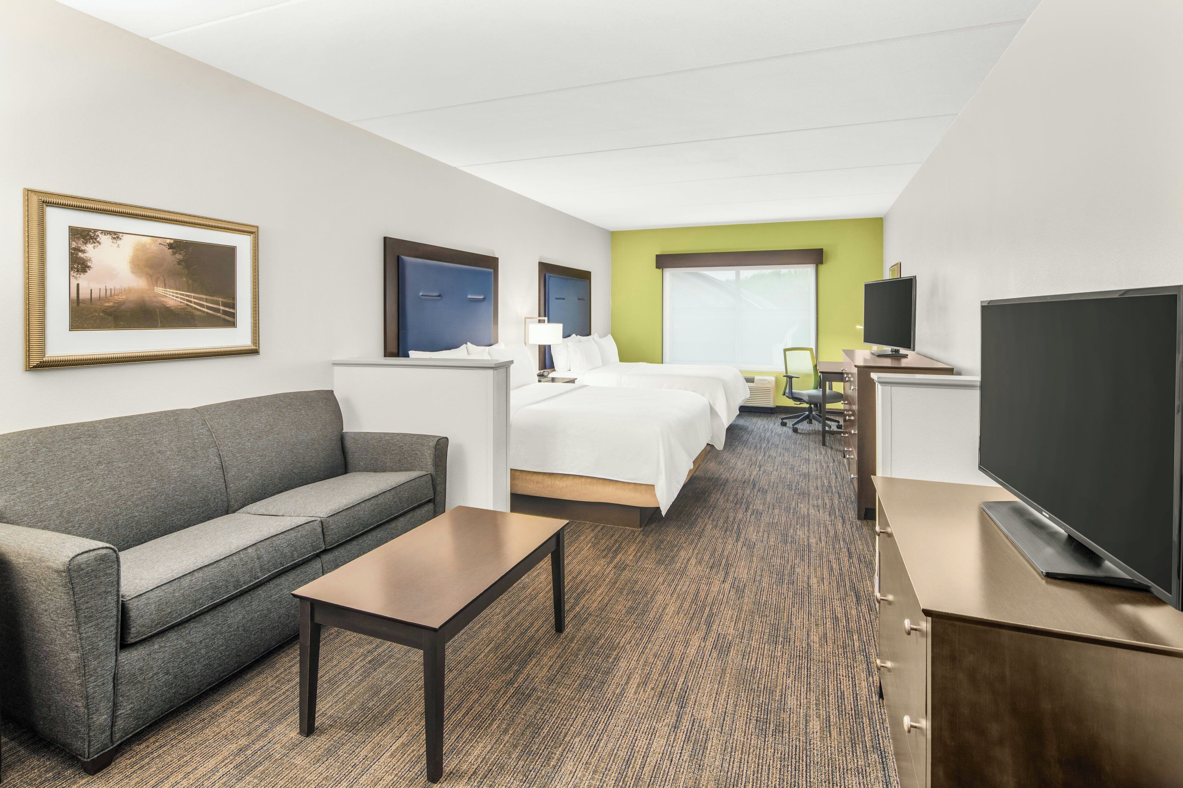 A hotel room with a sofa, a bed, a desk, a TV, and a framed picture on the wall.