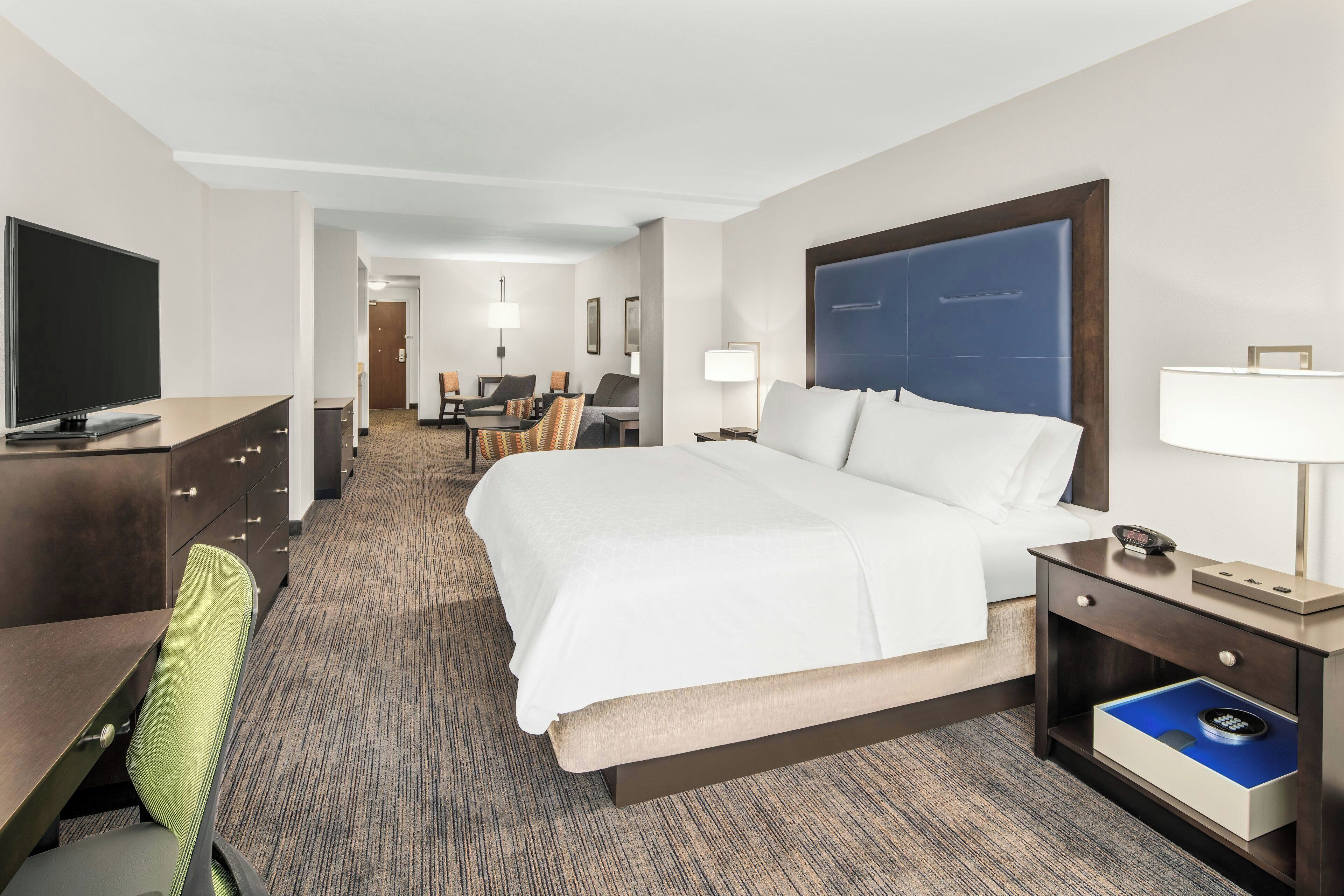 A hotel room with a bed, desk, chair, TV, and a desk lamp.