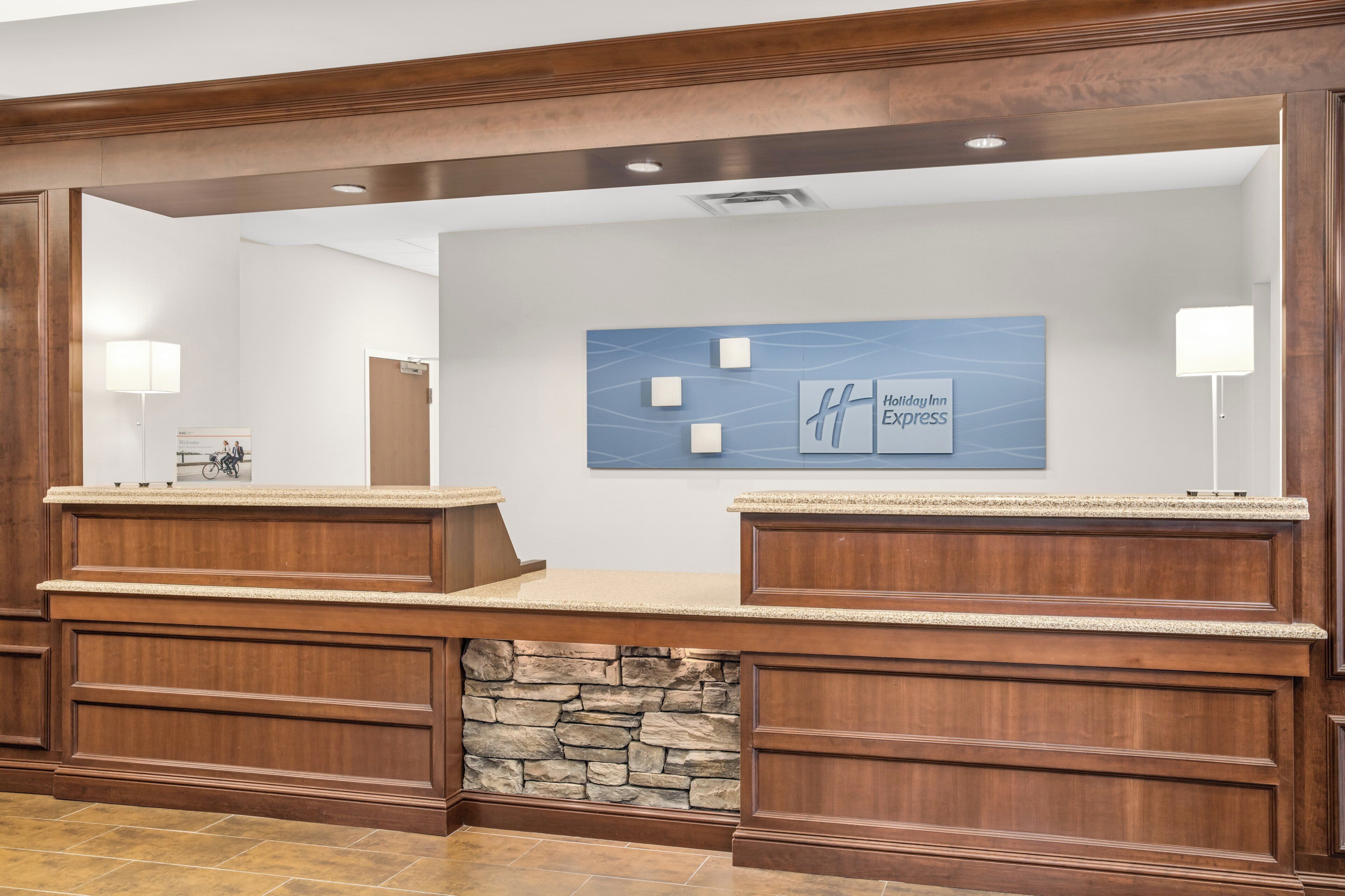 A reception desk with a stone accent wall, a blue wall with a logo, and two wall-mounted lamps.