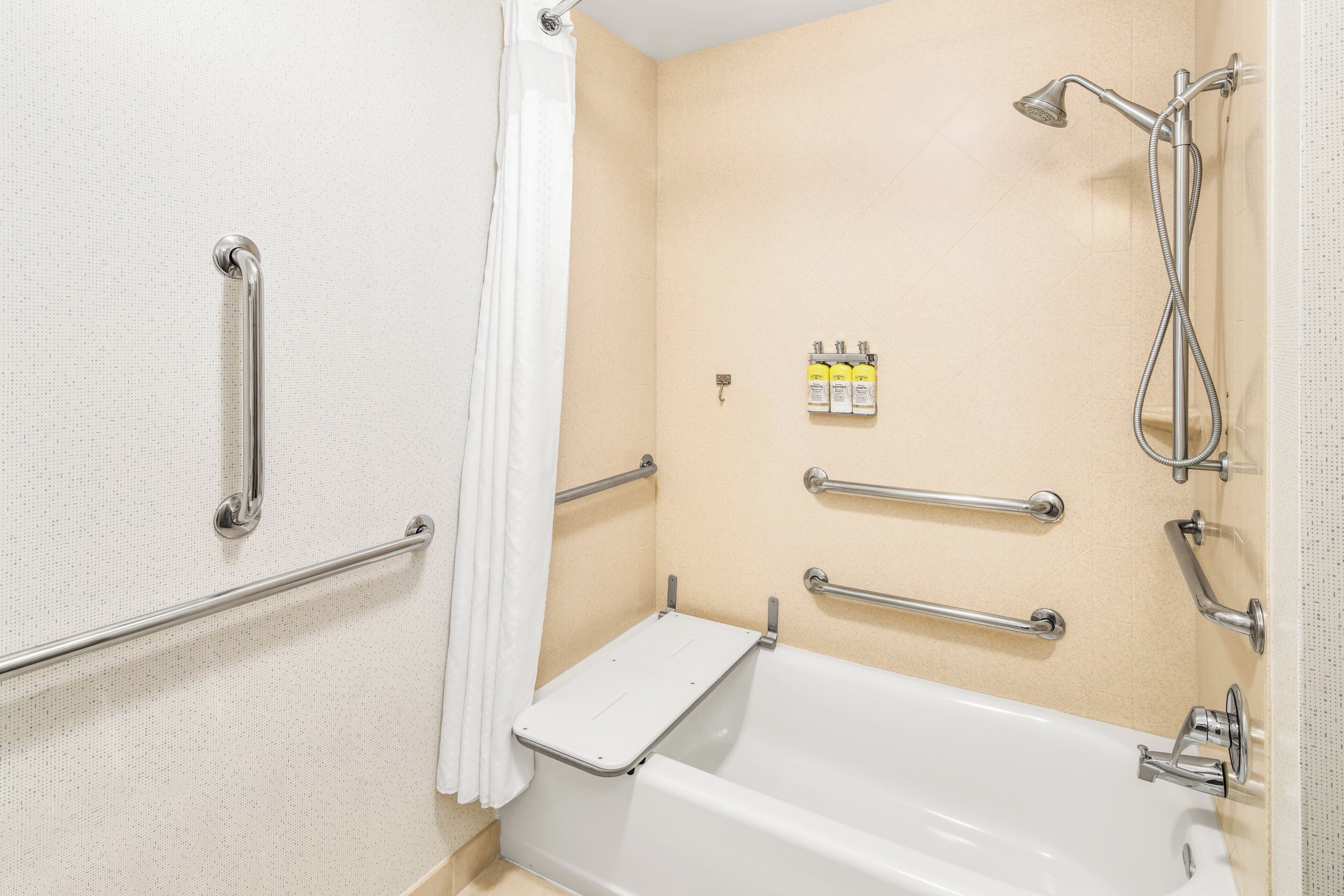 Un baño con bañera, barras de apoyo, cabezal de ducha y artículos de aseo.