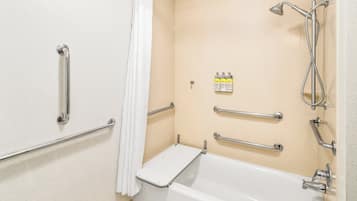 Un baño con bañera, barras de apoyo, cabezal de ducha y artículos de aseo.