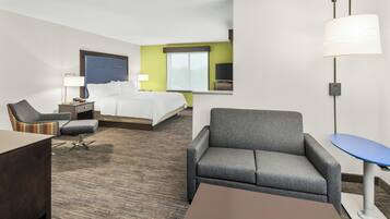 A hotel room with a bed, two armchairs, a desk, a lamp, a TV, and a window.