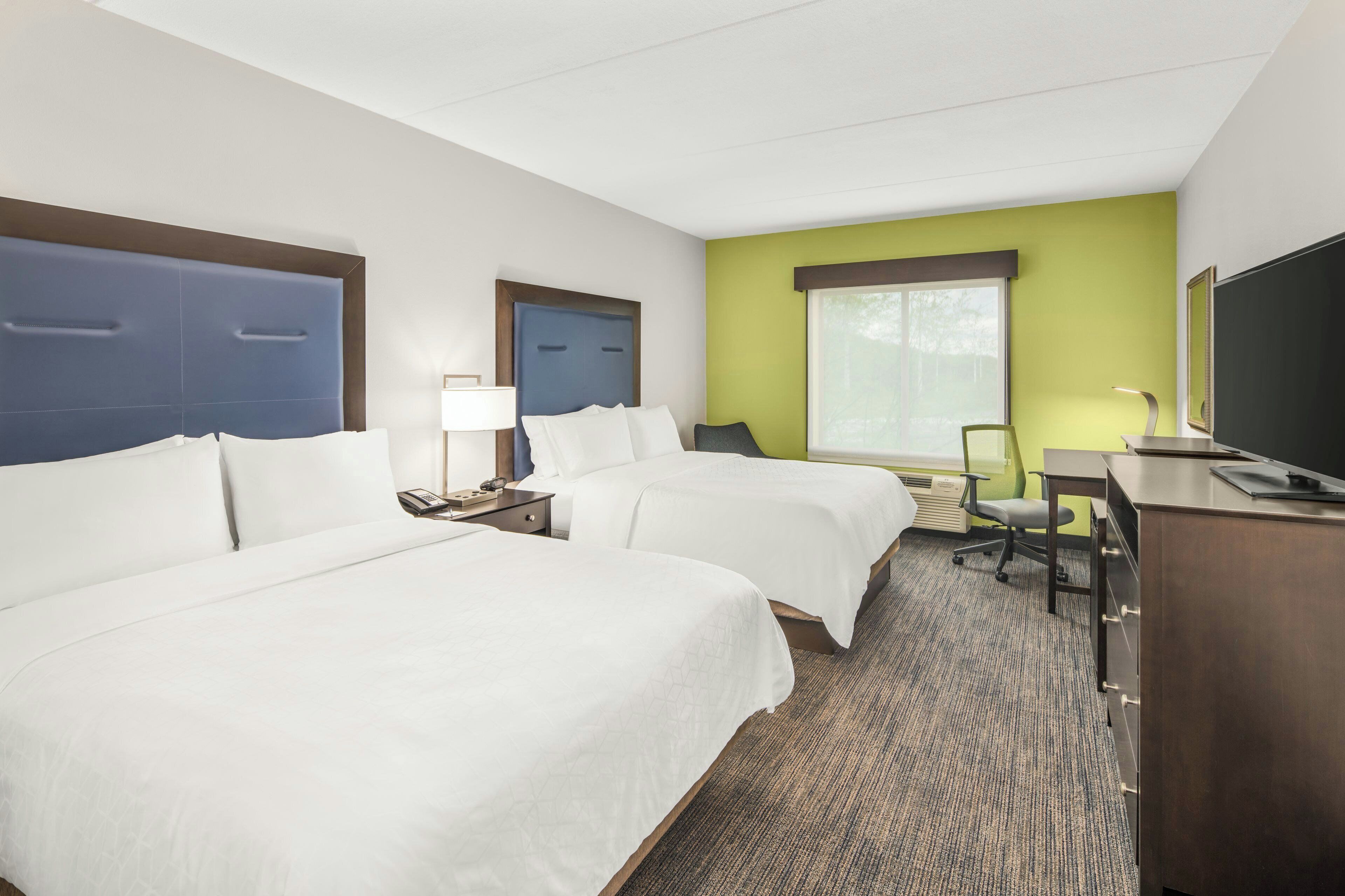 A hotel room with two beds, a desk, a chair, a television, and a window.