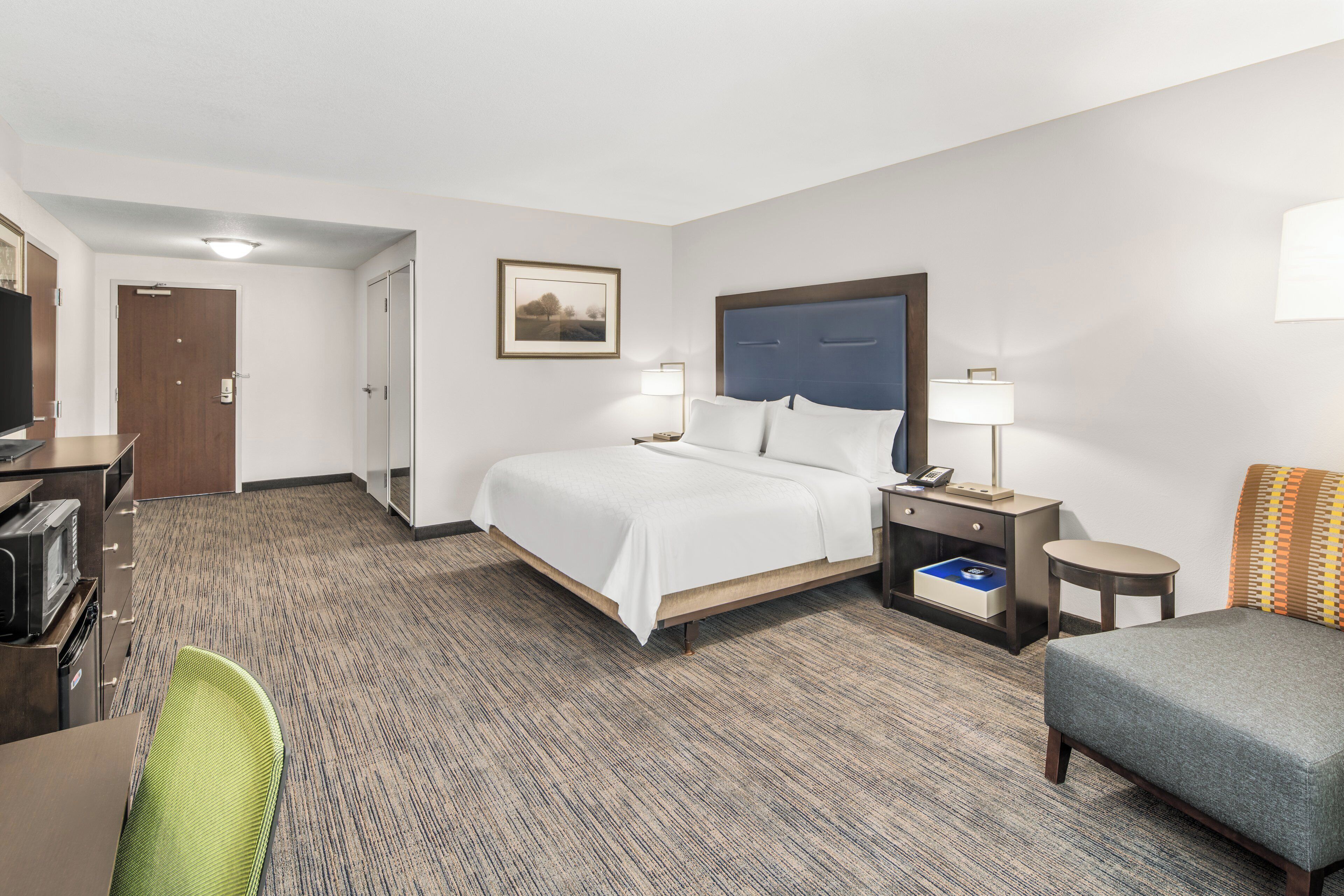 A hotel room with a bed, bedside tables, a desk with a television, and a chair.