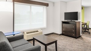Une chambre d’hôtel avec une grande fenêtre, un téléviseur à écran plat posé sur un meuble, une petite table, un canapé et une chaise.