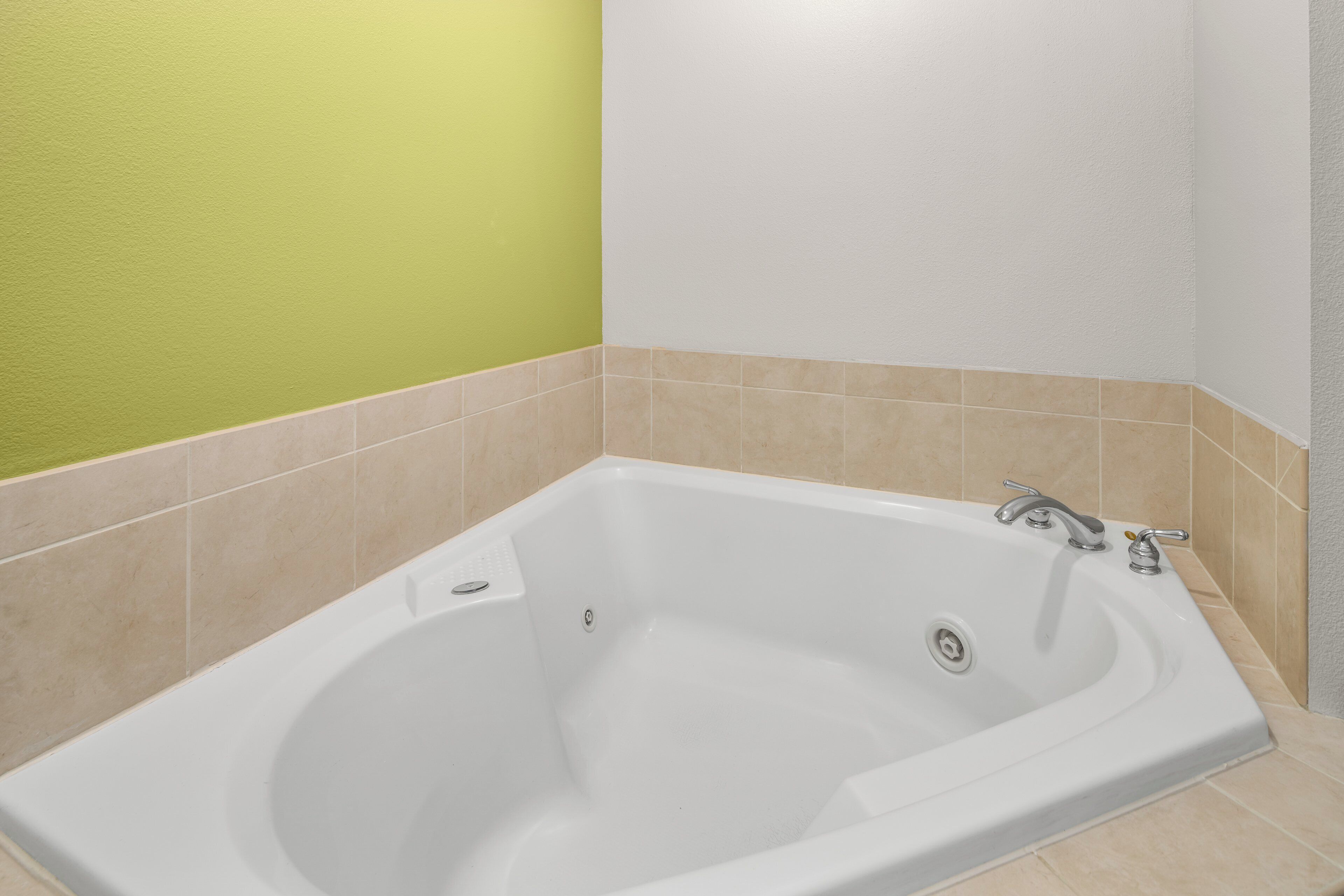 Un baño con una bañera blanca, azulejos color beige y una pared verde.