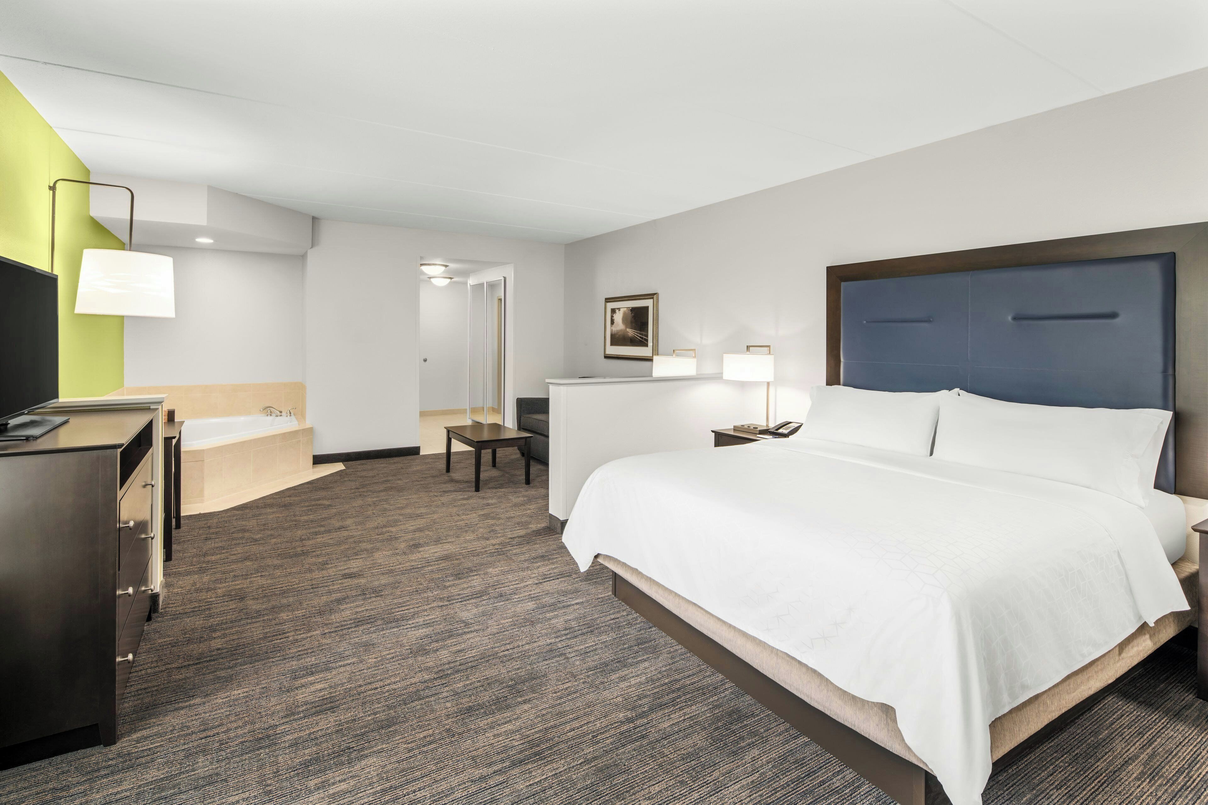 A hotel room with a bed, a desk, a chair, a lamp, a picture on the wall, and a bathroom with a bathtub and sink.