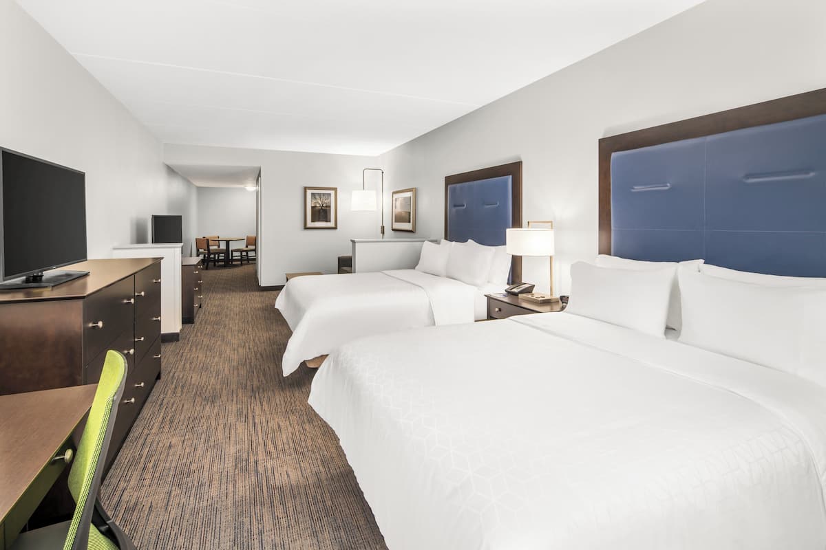 A hotel room with two beds, a desk, a chair, a TV, and a small table.