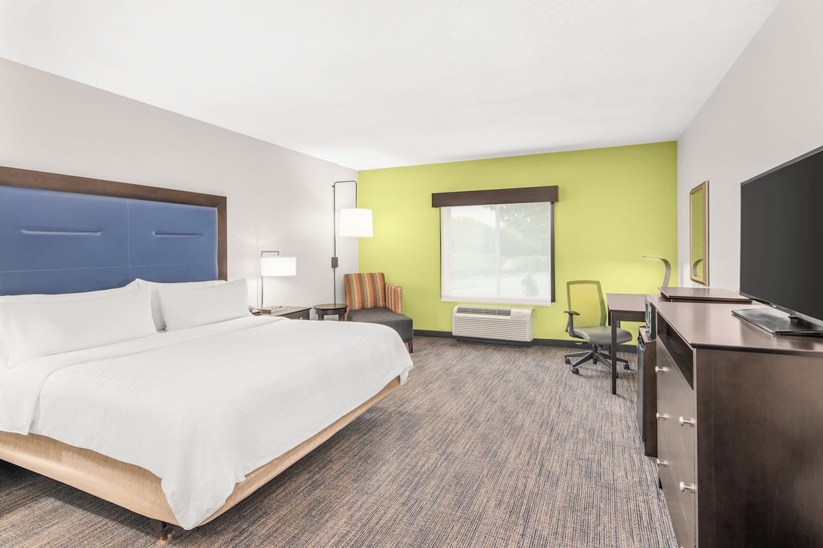 A hotel room with a bed, desk, chair, lamp, and TV.
