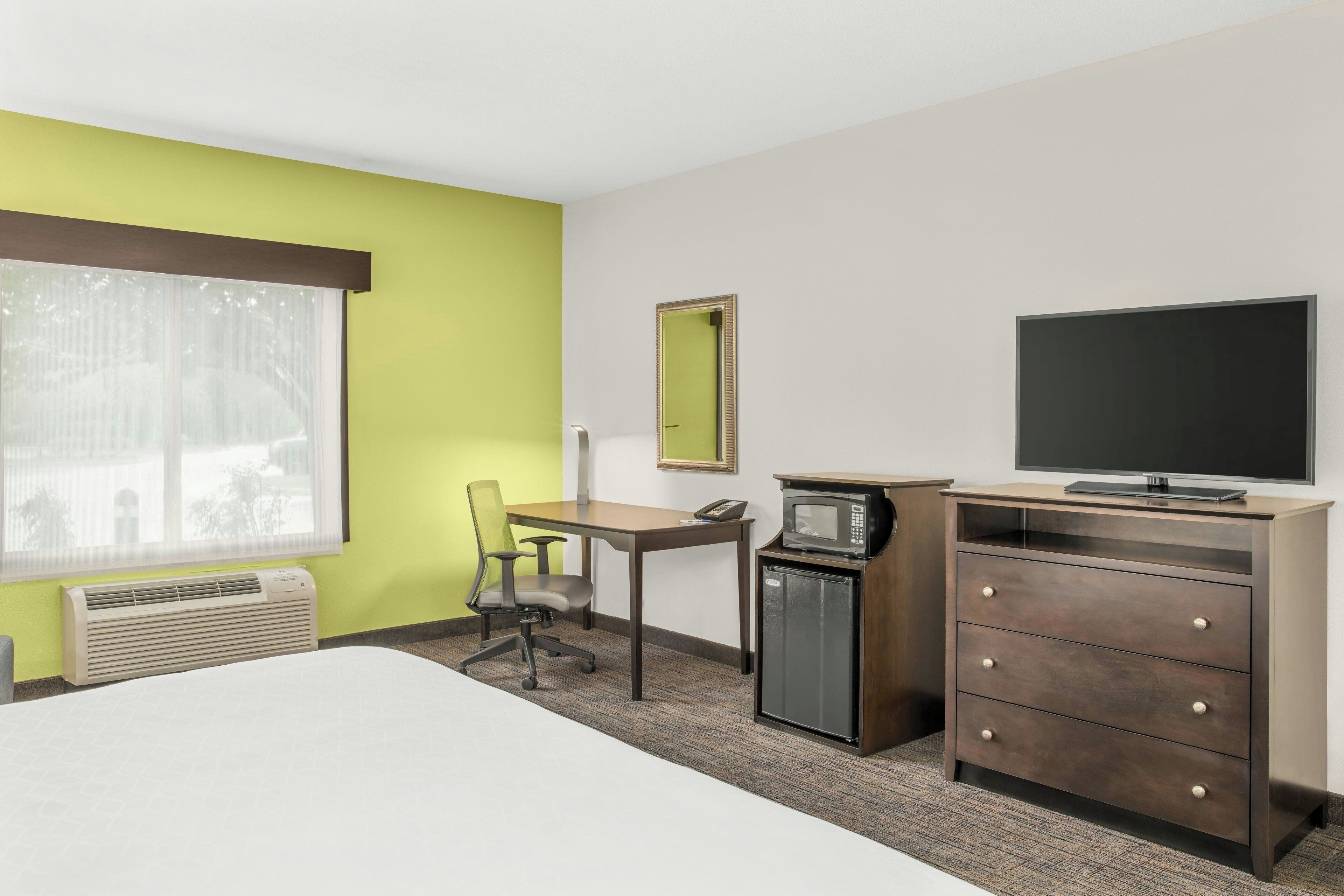 Quarto de hotel com cama, escrivaninha, cadeira, micro-ondas, televisão e cómoda.