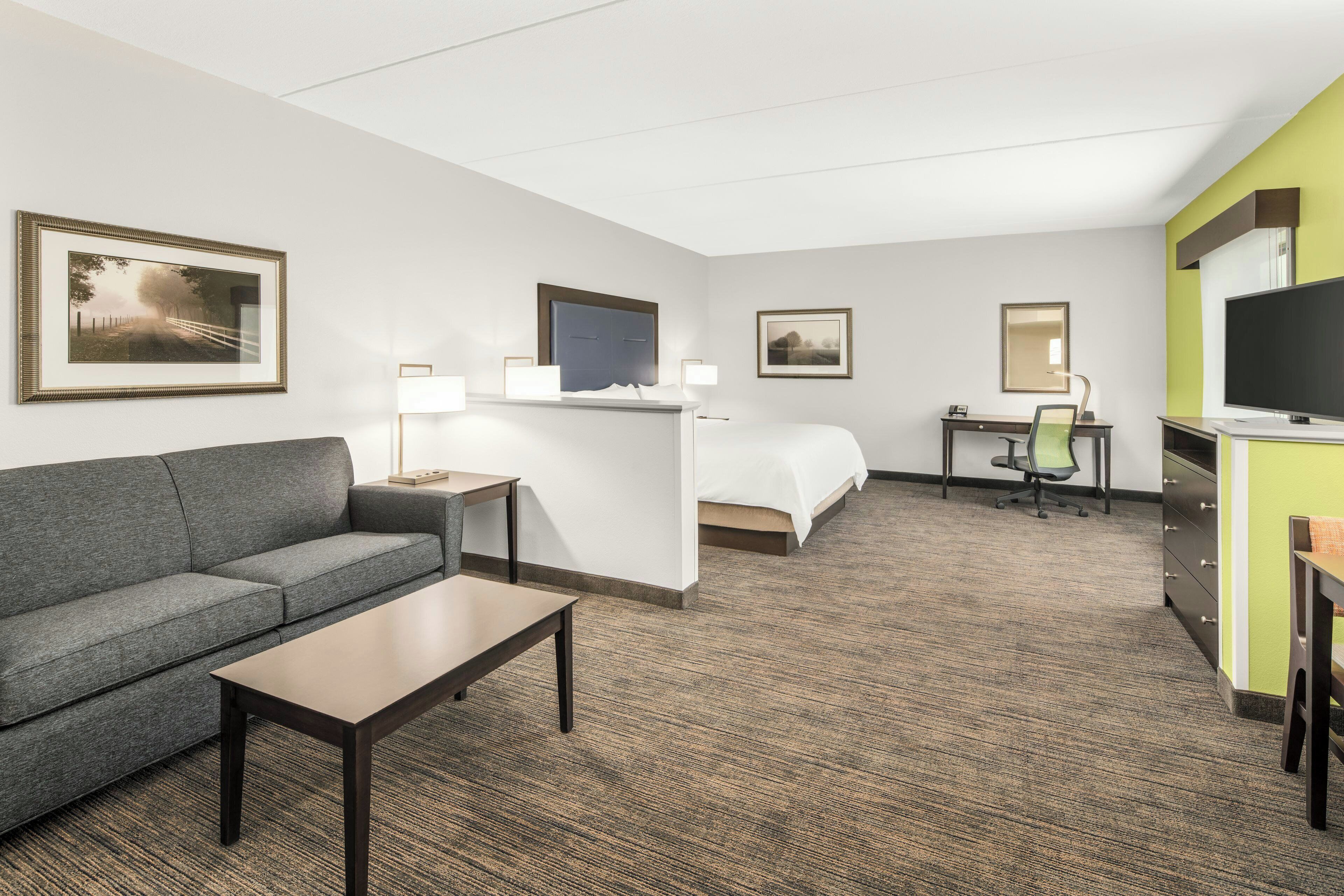 A hotel room with a sofa, a bed, a desk, a television, and framed pictures on the walls.