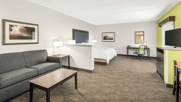 A hotel room with a sofa, a bed, a desk, a television, and framed pictures on the walls.