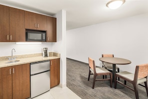 A compact kitchen with wooden cabinets, a built-in microwave, a coffee maker, and a dishwasher. There is a small dining area with a round table and two chairs.