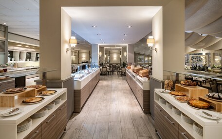 A modern hotel kitchen with a central island, multiple serving counters, and a long counter with baked goods.