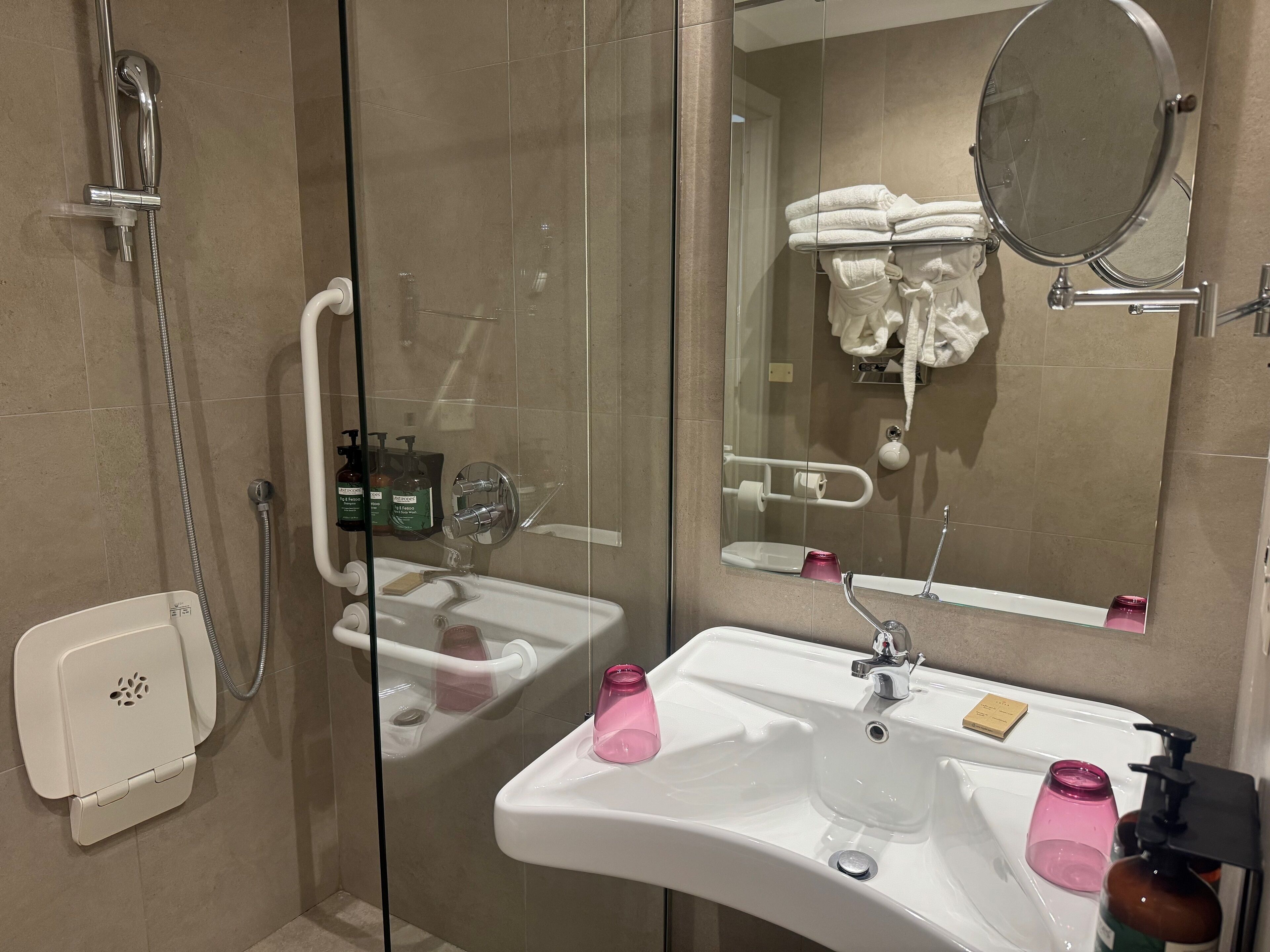 Une salle de bain moderne avec une douche à parois de verre, un lavabo blanc avec un miroir et des articles de toilette.