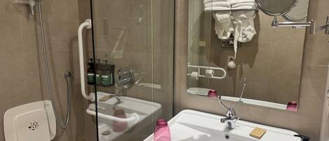 Un baño moderno con ducha envuelta en vidrio, lavamanos blanco con espejo y artículos de aseo.