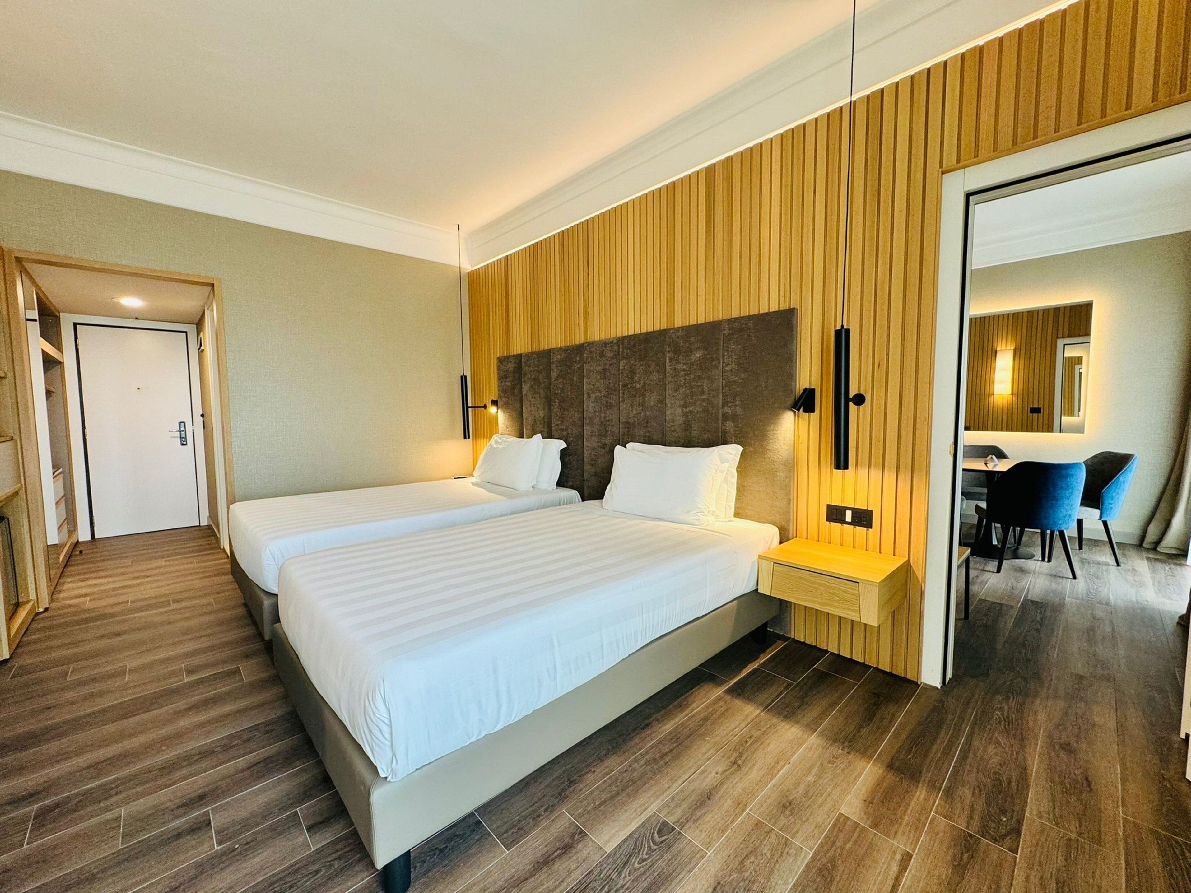 A hotel room with a large bed, bedside tables, a desk with chairs, and a mirror.