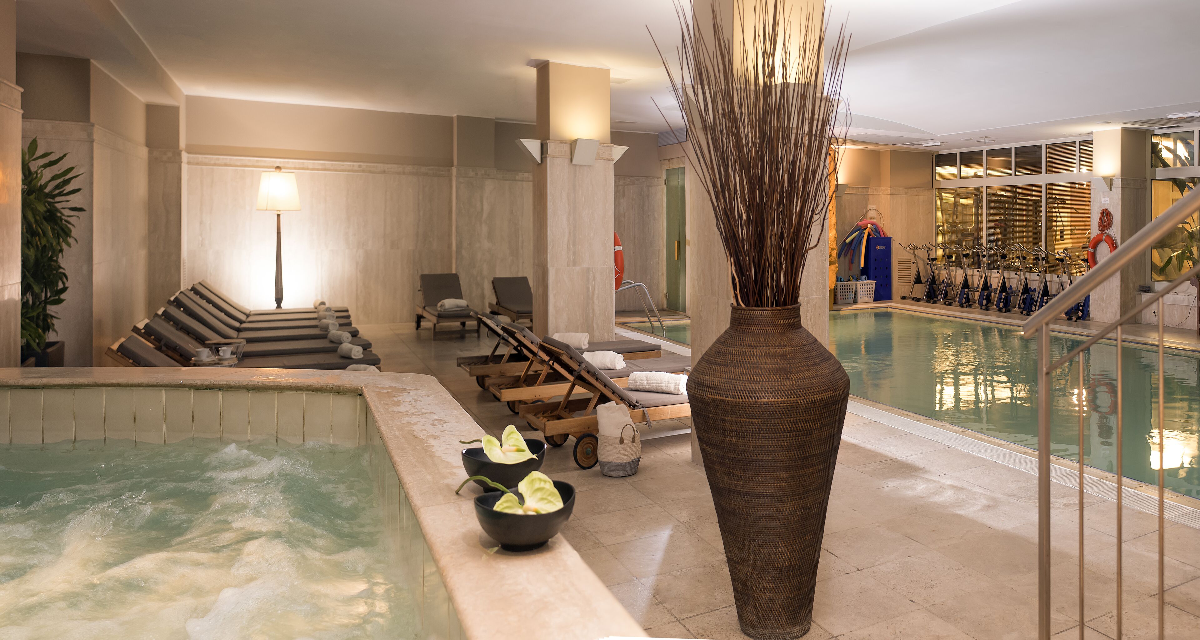 A spa area with a hot tub, lounge chairs, a large vase, and a pool.